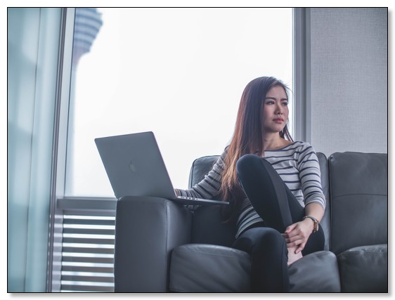 Picture of a young woman with a laptop sitting on a couch looking pensive, communicating the need for dementia training to have healthy relationships. 